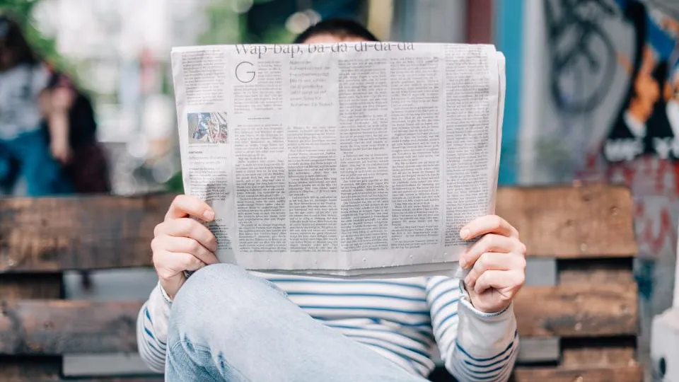 Pessoa lendo jornal sentada num banco